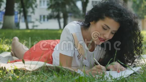 漂亮的卷发黑发女郎在公园里的格子上放松写了一封信视频的预览图