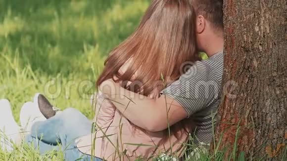 一对相爱的情侣拥抱在一起坐在公园的树下后视图视频的预览图