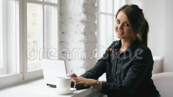 年轻微笑的女学生坐在咖啡店的桌子上手提电脑在室内视频的预览图