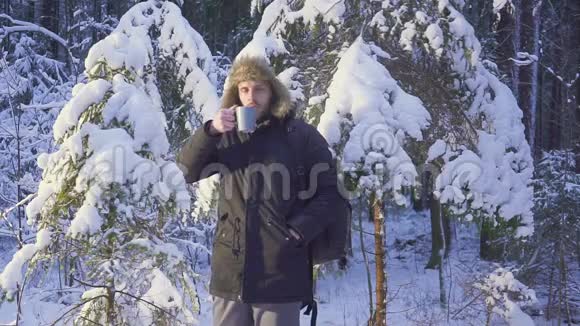 一个年轻人在冬天的森林里喝热茶冬天森林里阳光明媚的早晨那个人看了看视频的预览图