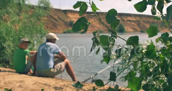 一对幸福的父子坐在河岸上钓鱼爸爸和儿子早上在钓鱼家庭幸福视频的预览图