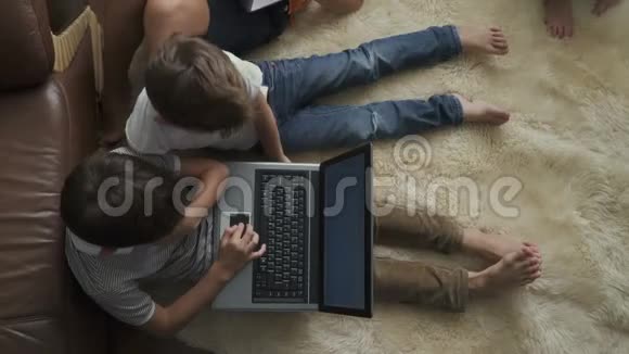 两个男孩坐在地毯上玩笔记本电脑视频的预览图