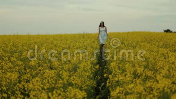 美丽的女孩走在黄花的田野里微笑和欢笑视频的预览图