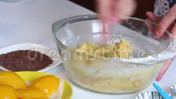 女人在面团中加入面粉用勺子在玻璃容器中搅拌下一个盘子是磨碎的巧克力和桃子视频的预览图