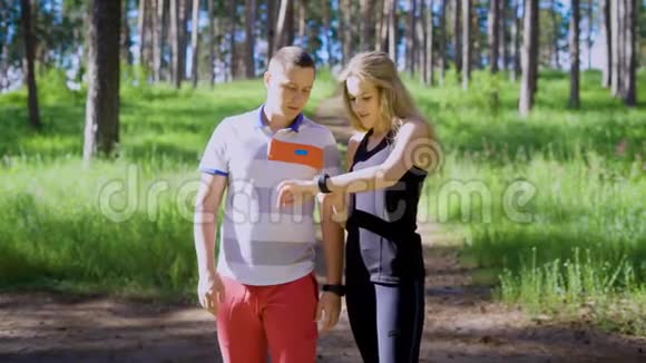 阳光明媚的一天一对身穿运动服的年轻夫妇穿过森林一个女运动员问一个男人他们有多远视频的预览图