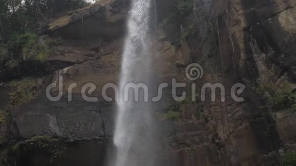 泡沫的水从绿树上的褐色岩石悬崖上落下视频的预览图
