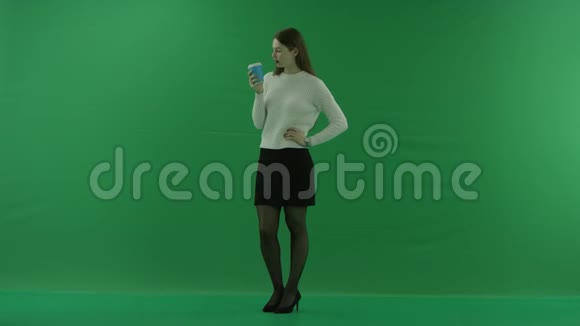 女孩站在一个半转弯的地方看着左边从绿色屏幕上的一个杯子里喝东西视频的预览图