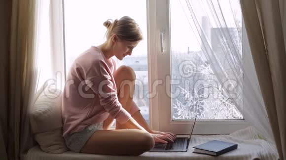 可爱的女人用她的笔记本电脑坐在窗台上视频的预览图