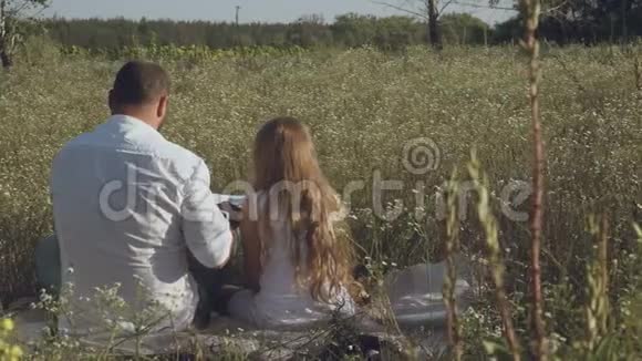 带着小女孩的男人正在草地上翻书在格子布上放松视频的预览图