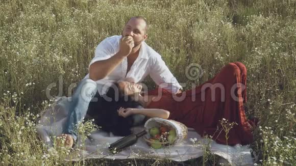 可爱的情侣在田边的格子布上放松人们吃一个苹果视频的预览图