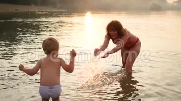 祖母和孩子在海上玩耍造成了水的飞溅娱乐和户外游戏日落时间视频的预览图
