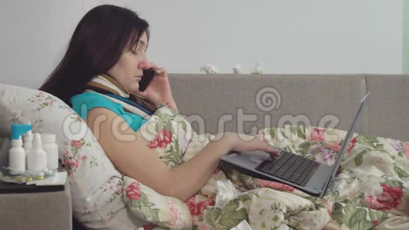 生病的女人躺在家里的床上用电话和笔记本电脑工作视频的预览图