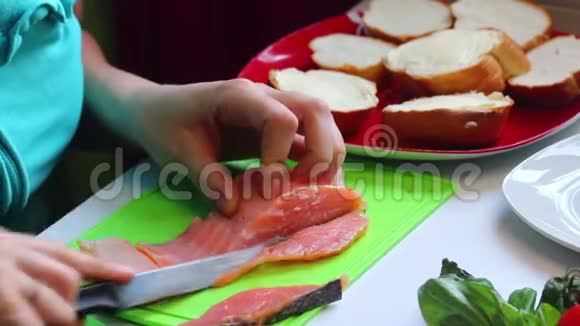 一个女孩切三文鱼做三明治盘子旁边是一块切片面包和草药白色背景的特写视频的预览图
