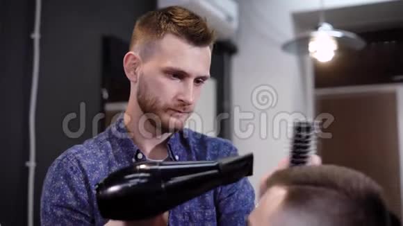 时尚男理发师的形象使用吹风机在理发店做现代理发年轻人把客户吹干视频的预览图