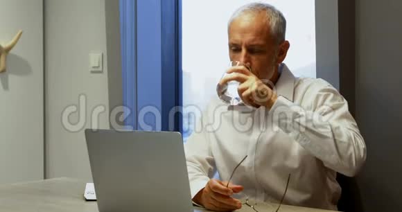 一个商人在使用笔记本电脑4k时喝了一杯水视频的预览图