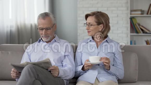 老年夫妇坐在沙发上男人看报纸女人喝茶做广告视频的预览图