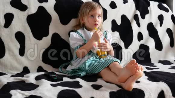 儿童喝橙汁坐在沙发上小女孩看电视儿童视频的预览图