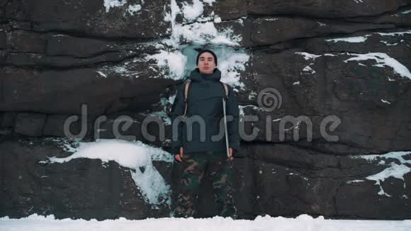 站在白雪覆盖的岩壁前的年轻人视频的预览图