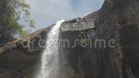 泡沫的水从绿树上的褐色岩石悬崖上落下视频的预览图