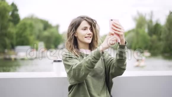 穿绿衣服的年轻女子在河边的桥上自拍视频的预览图