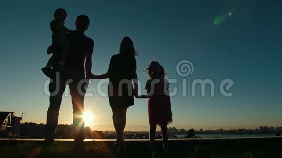 全家人的肖像父亲母亲女儿和小儿子日落时的轮廓在天际线前视频的预览图