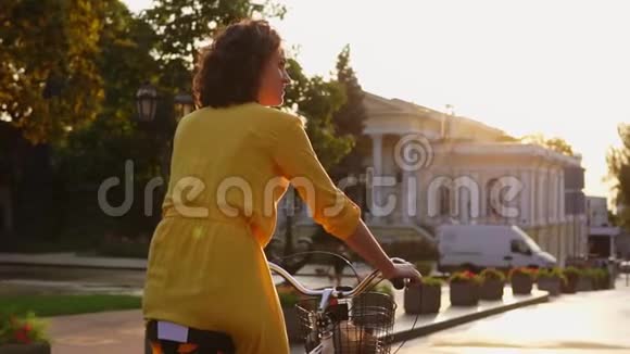 一个美丽的女人骑着一辆城市自行车在市中心有一个篮子和花显示她的拇指向上贷款视频的预览图