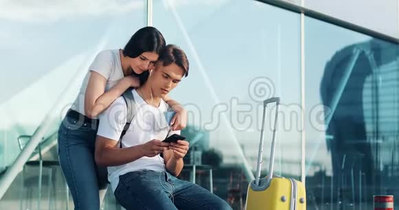 使用智能手机相爱的幸福夫妇年轻的已婚夫妇在机场等待航班时玩得很开心那个女人视频的预览图