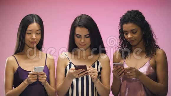 穿着睡衣的女性朋友在智能手机上聊天在粉红色背景下被隔离视频的预览图