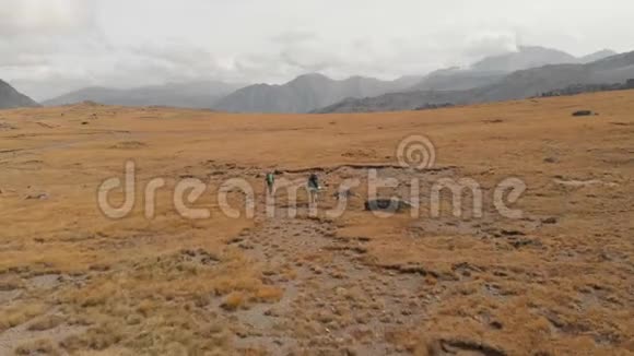 一对戴着帽子和太阳镜的大背包的旅行者男女在高山上漫步的鸟瞰图视频的预览图