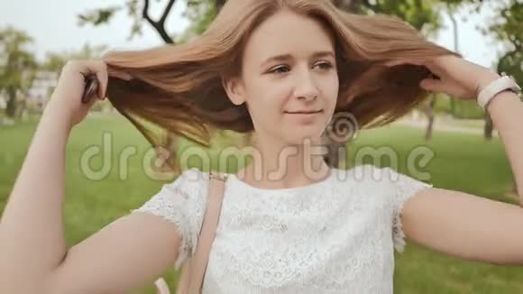 美丽的学生女孩微笑着在公园里梳着长发在学习期间休息视频的预览图