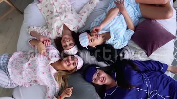 四个穿着睡衣微笑的女人躺在床上直接看着相机在睡衣派对伴娘视频的预览图