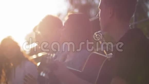 年轻的白种人朋友在夏天的公园里玩在日落时用吉他唱歌视频的预览图