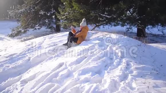一个少女在冬天的雪园里从山上滑下来一只狗在雪地里和一个快乐的女孩玩耍阳光明媚的霜天视频的预览图