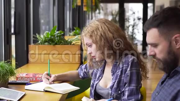 一位年轻女子向一位年轻男子解释了一本书中一个复杂的材料她坐在咖啡馆里视频的预览图