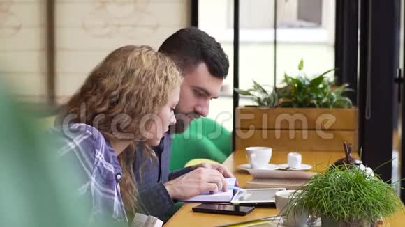 一对夫妇在咖啡馆里用平板电脑和笔记本计划他们的一周视频的预览图