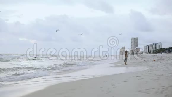 一个快乐的小男孩沿着海滩跑4k视频的预览图