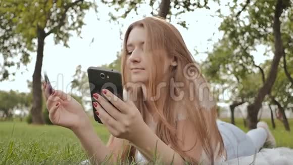 躺在大自然中的一位年轻女孩用笔记本电脑用信用卡通过互联网购物视频的预览图