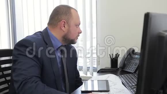 男老板坐在现代办公室里用电脑和平板电脑工作视频的预览图