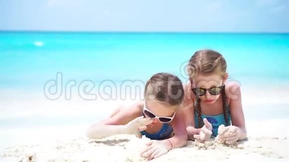 可爱的孩子们在白色的海滩上玩沙子两个女孩在暑假玩得开心视频的预览图