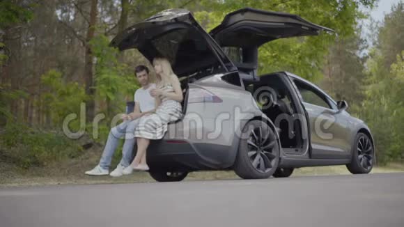 恋爱中的年轻夫妇坐在电动车的后备箱里聊天视频的预览图