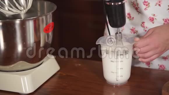 女人在厨房桌子上用电动搅拌器将奶油混合在杯子里视频的预览图