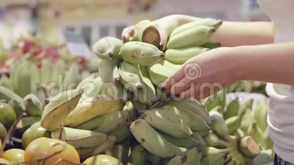 女人在超市挑选绿色香蕉从杂货店里拿一串香蕉的女人女孩视频的预览图