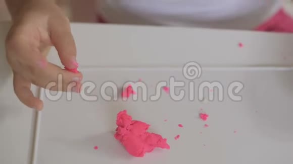 一个小女孩坐在一个房间的桌子上用粉红色的塑料制成雕像手和手指的特写视频的预览图