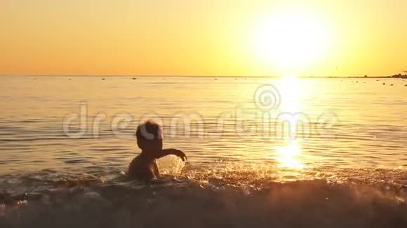 快乐男孩在海上嬉戏的剪影日落时升起水花动作缓慢视频的预览图