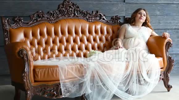 穿着豪华礼服的怀孕新娘正坐在皮沙发上视频的预览图