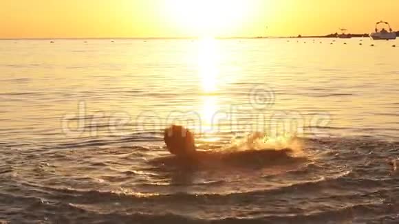 快乐男孩在海上嬉戏的剪影日落时升起水花动作缓慢视频的预览图