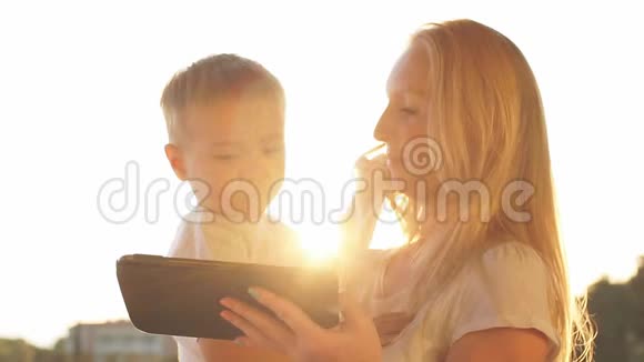 母亲和儿子在日落时使用平板电脑度假视频的预览图