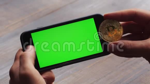 人使用水平智能手机与绿色屏幕男子手手机和一枚金比特币的特写镜头视频的预览图