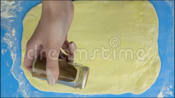 4K镜头面包师把一层肉桂洒在生糕点面团上顶部视图视频的预览图