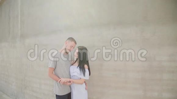 一对相爱的夫妇在混凝土墙的背景下拥抱和亲吻视频的预览图